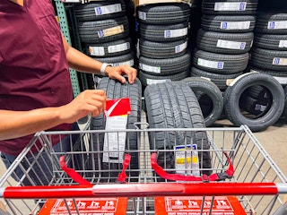 Person holding a BJ's membership card by a cart that is holding two good year tires