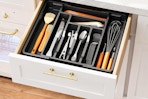 A drawer is open to reveal an expandable silverware organizer full of organized silverware.