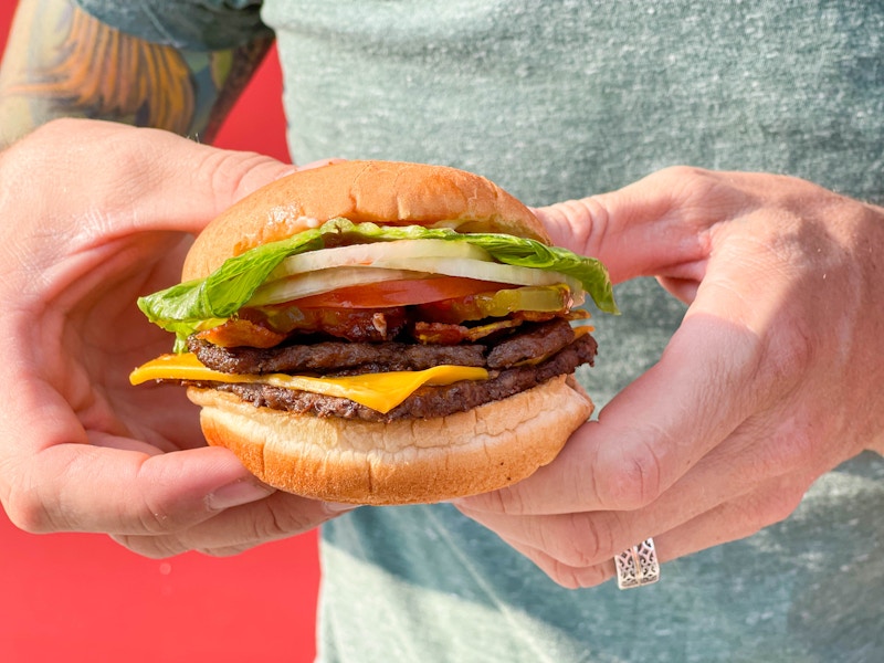 A person holding a Wendy's double stack burger outside of a Wendy's.