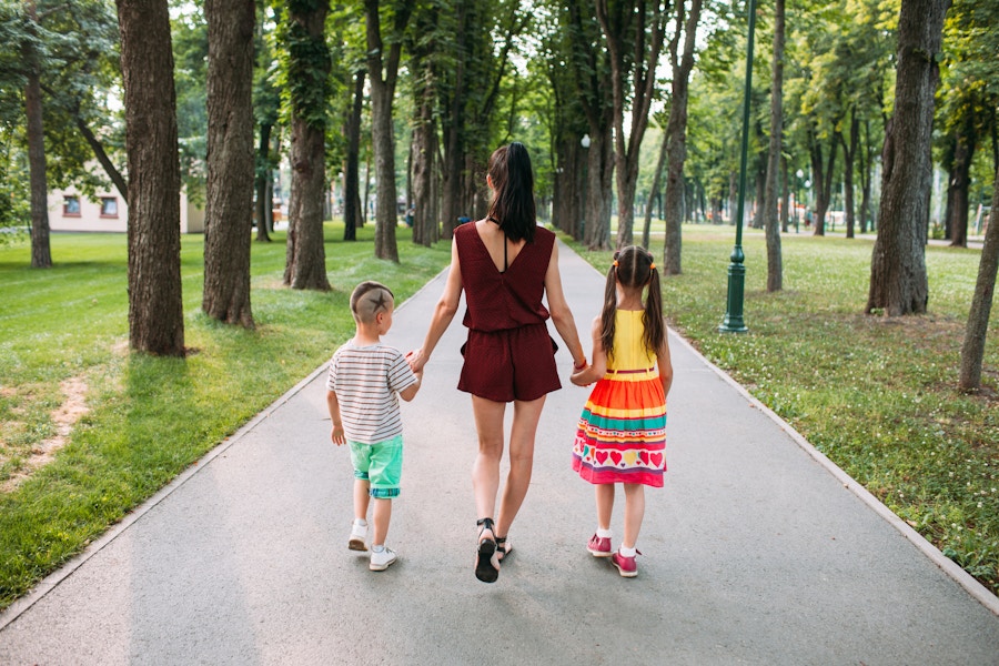 A parent walking through a park, holding the hands of two children