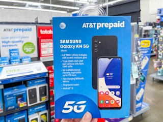 A prepaid Samsung Galaxy A14 5G held out by hand in front of a store aisle.