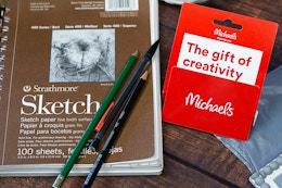 a michaels gift card next to a sketchbook and drawing pencils