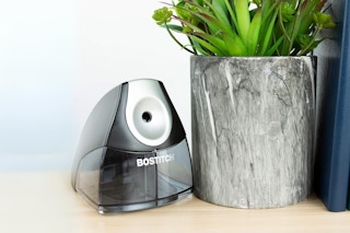 A Bostitch electric pencil sharpener sits on a desk next to a plant and a book.