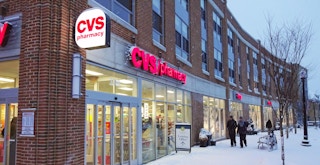 People walking on a snowy sidewalk by a CVS store.