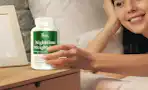 a person holding a bottle of supplements next to their bed