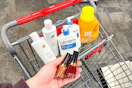 person holding revlon nail polish over a cart with dove shampoo, lubriderm lotion, and arm & hammer detergent in it