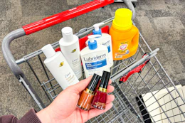 person holding revlon nail polish over a cart with dove shampoo, lubriderm lotion, and arm & hammer detergent in it