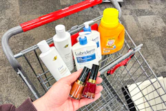 person holding revlon nail polish over a cart with dove shampoo, lubriderm lotion, and arm & hammer detergent in it