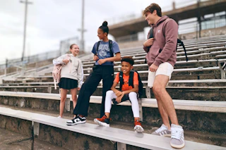 Lifestyle image of a group of kids wearing backpacks outside in front of bleachers