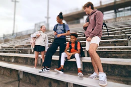 Lifestyle image of a group of kids wearing backpacks outside in front of bleachers