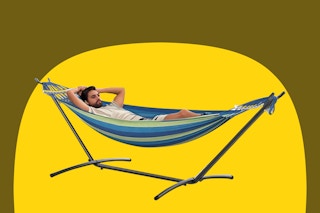 A man lies in a hammock on a metal stand. The hammock holds 2 people or 500 pounds. It's striped blue and green