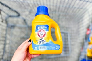 hand putting a bottle of arm hammer detergent in shopping cart