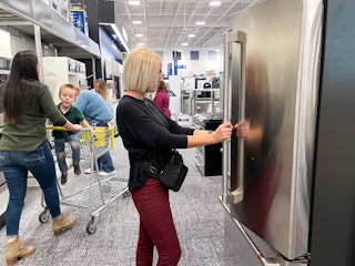 A group of people shopping in the appliance section at best buy.