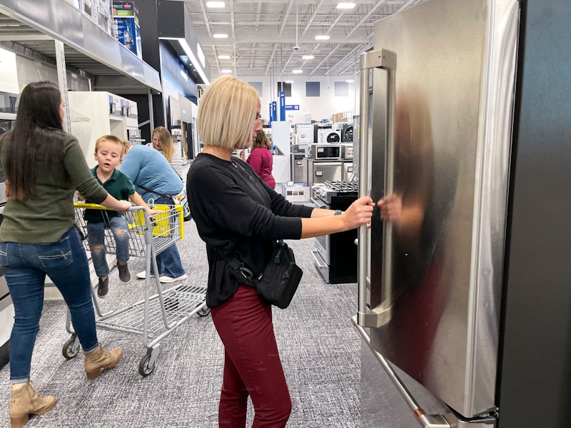 A group of people shopping in the appliance section at best buy.