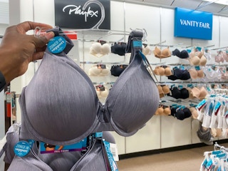 someone holding a bra on a hanger on a rack full of bras in the bra section