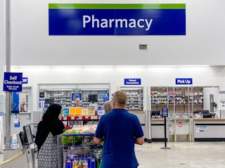 a man and a woman with a shopping cart full of groceries standing in front of the pharmacy at sam's club