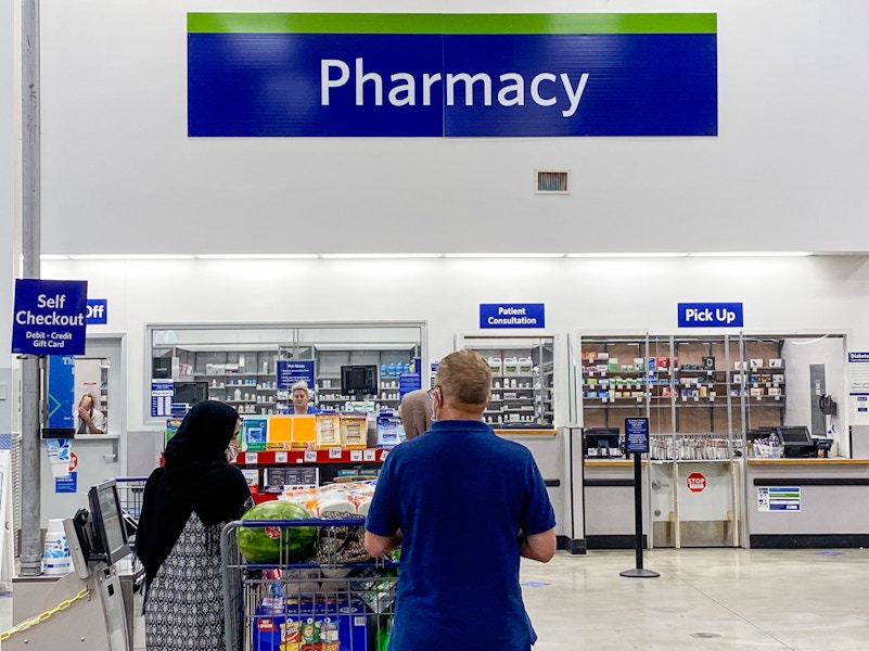 a man and a woman with a shopping cart full of groceries standing in front of the pharmacy at sam's club