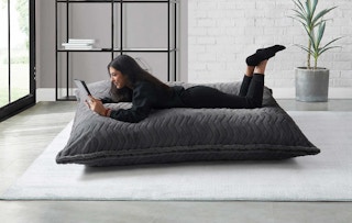 women reading a book on an oversized floor pillow in a living room