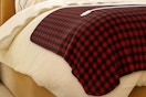 Lifestyle image of a red plaid Sunbeam Heated Microplush Blanket on bed