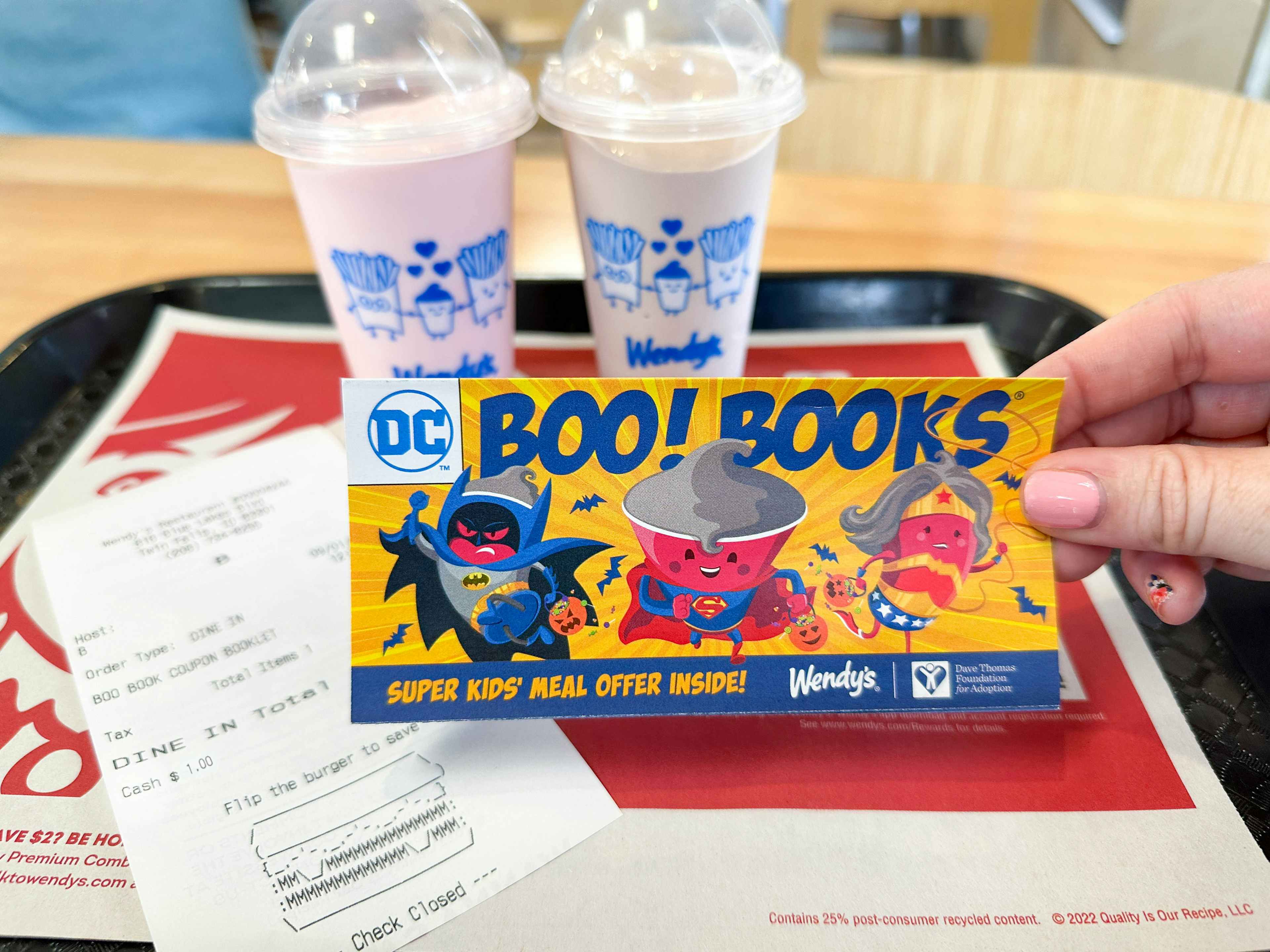 a person holding a wendys boo books in front of two frostys and receipt on tray 