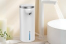 A tall white cylindrical automatic soap dispenser next to a white sink