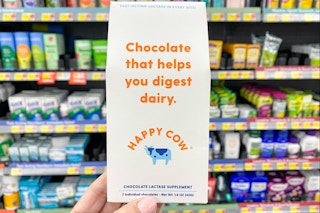 person holding a pack of happy cow lactase supplement in front of a shelf