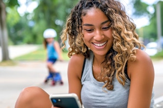 a mom on her phone with a child rollerskating in the background