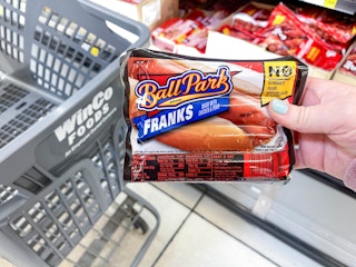 a person holding up ballpark hot dogs in front of cart