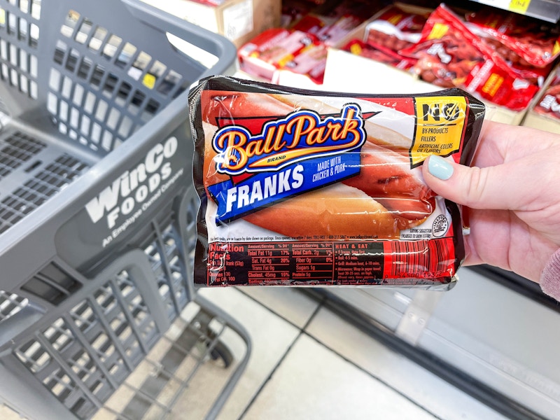 a person holding up ballpark hot dogs in front of cart