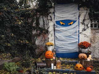 A front door decorated to look like a mummy with Halloween decorations on the steps leading up the porch.