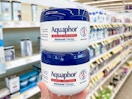 Two Aquaphor jars held out by hand, stacked on top of each other.