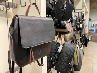A fossil bag with other purses and backpacks hung on hooks inside a DSW store.