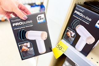 person holding a massage gun by the display shelf with a 50% off sign