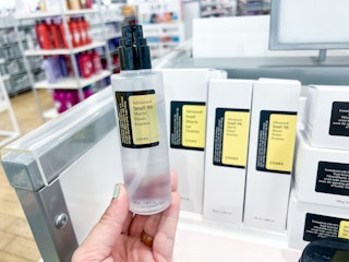a hand holding a bottle in front of a store shelf with products on it