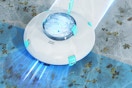 Round robotic pool cleaner with a clear window in the middle glides across several surfaces at the bottom of a pool.