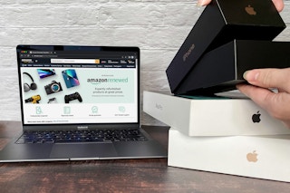 Some refurbished electronics on a table next to a laptop displaying the Amazon Renewed webpage