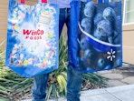 a person holding two reusing grocery bags from winco and walmart