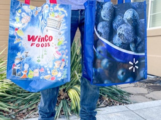 a person holding two reusing grocery bags from winco and walmart