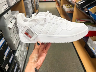 A woman's Adidas sneaker held out in front of a store aisle by hand.