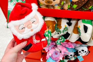 hand holding a squishmallow santa slipper in front of a display