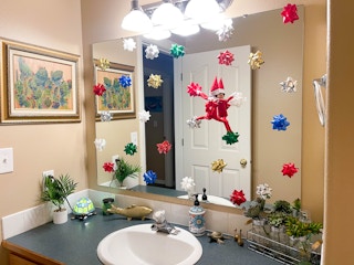 elf on the shelf doll climbing bathroom mirror with Christmas bows on mirror 