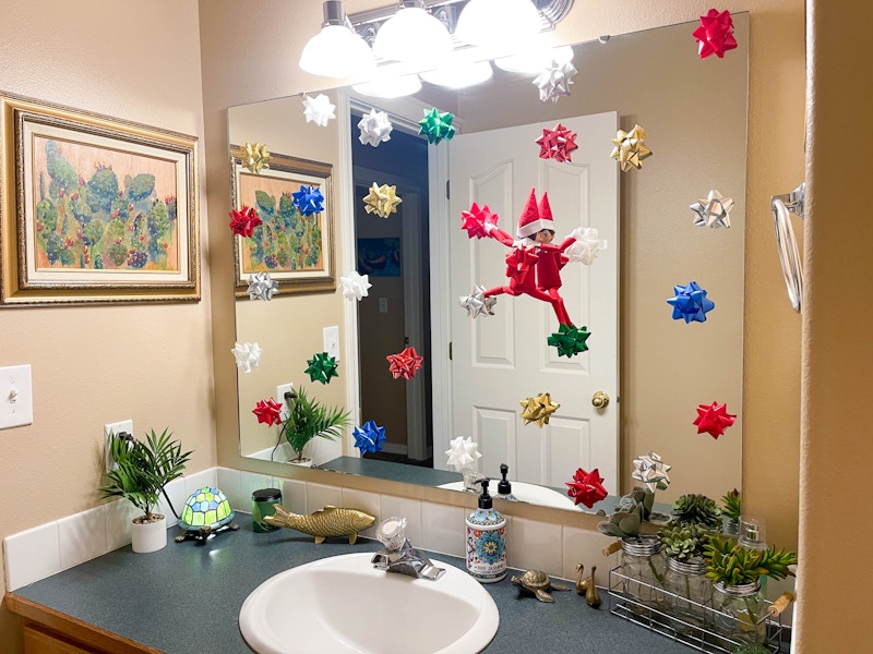 elf on the shelf doll climbing bathroom mirror with Christmas bows on mirror 