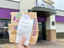 Someone holding up a Taco Bell Bag in front of a Taco Bell