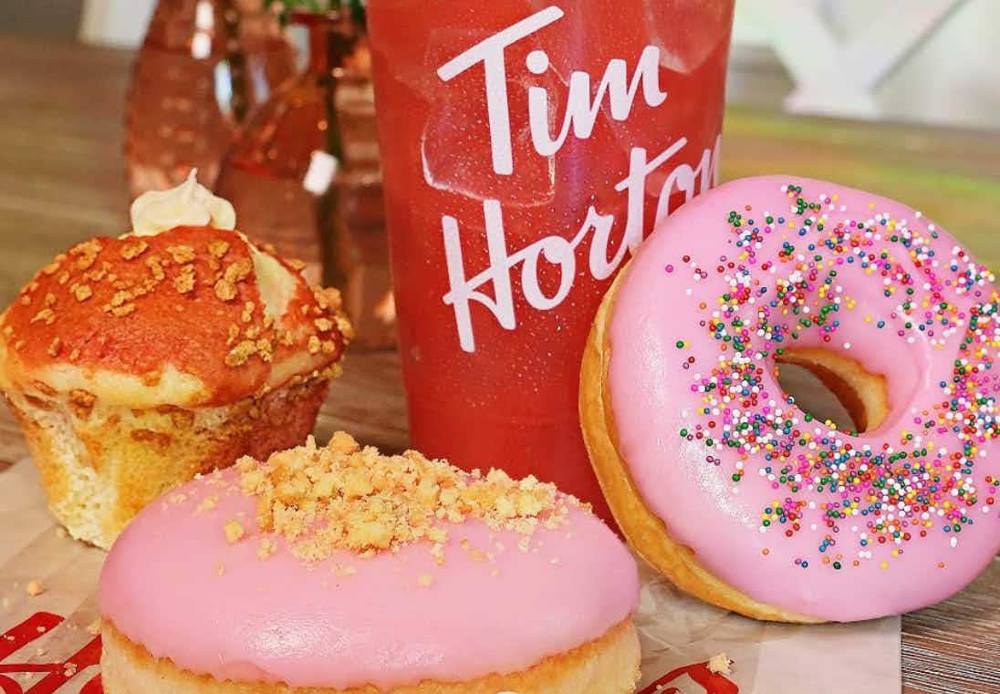 Some doughnuts from Tim Hortons sitting on a table next to a Tim Hortons to-go coffee cup.
