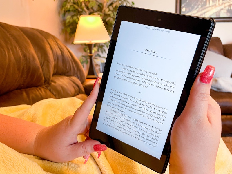 A woman's hands holding an Amazon Kindle displaying the first chapter of a book.