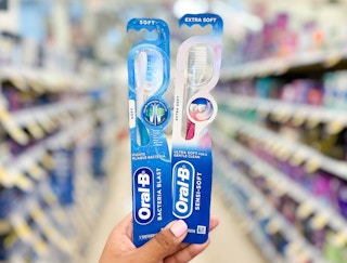 Hand holding two Oral-B toothbrushes in center of aisle