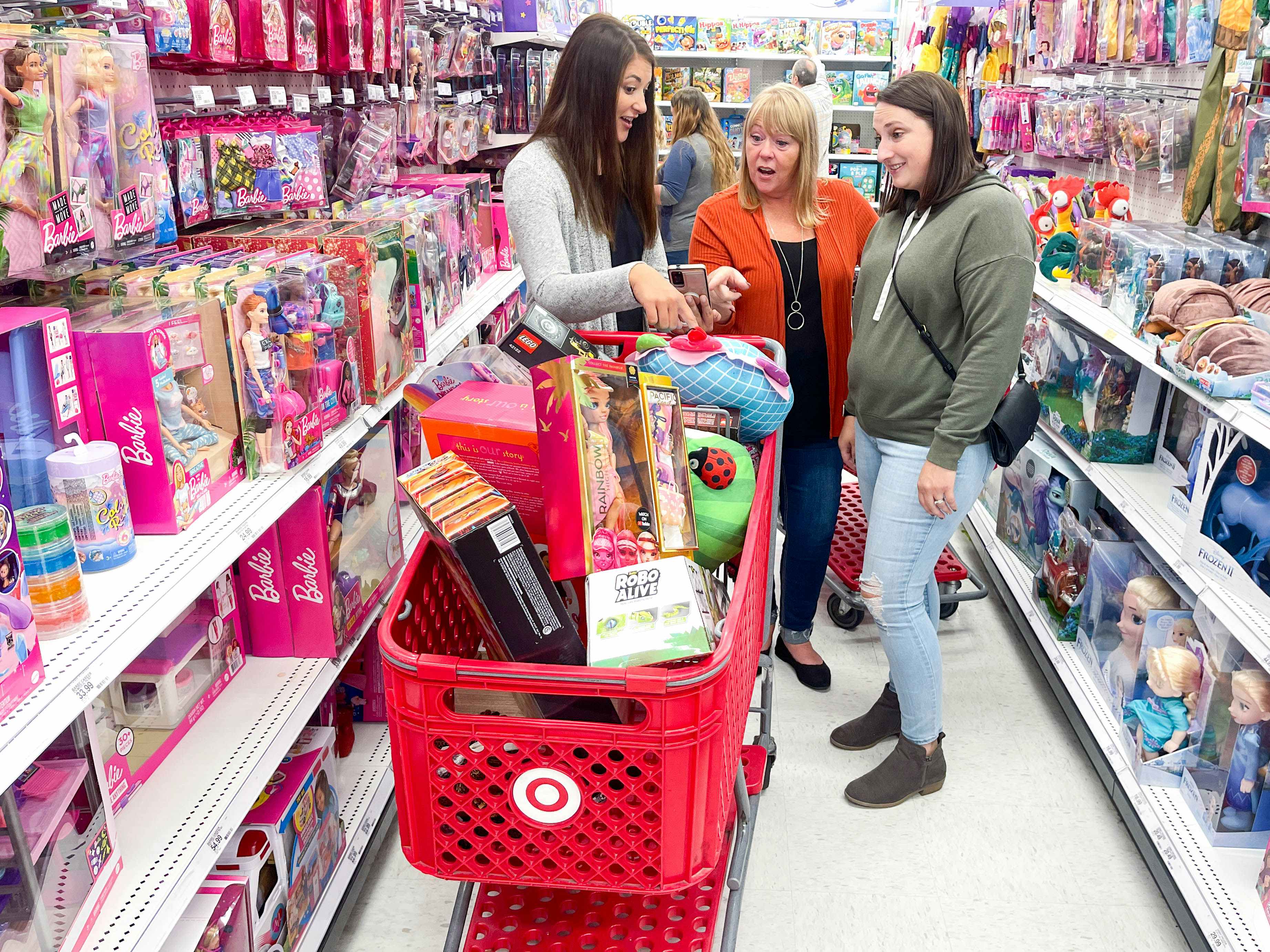 three women chatting in the toy aisle at target with a red shopping cart full of toys in front of them