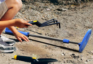 a blue metal detector on sand with a kid holding a mini rake