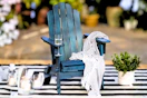 Lifestyle image of a navy wood Adirondack chair in an outdoor setting on a striped rug 