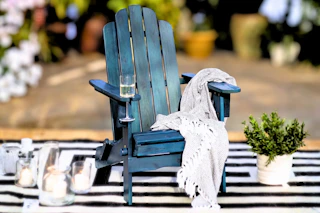 Lifestyle image of a navy wood Adirondack chair in an outdoor setting on a striped rug 
